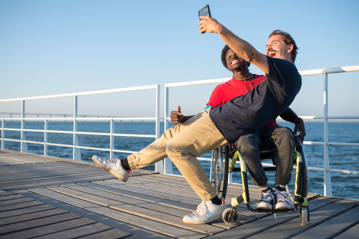 A wheelchair user taking a selfie on the boardwalk with a friend